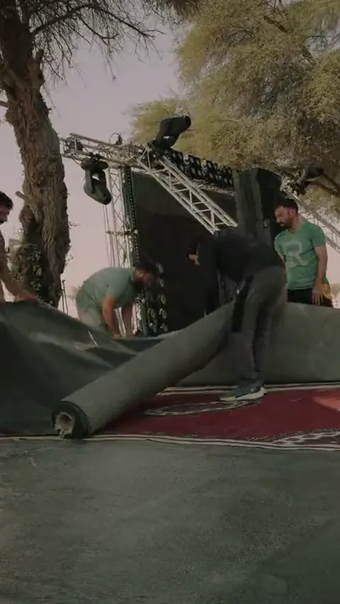 Crew rigging a stage and laying carpet at a desert event site