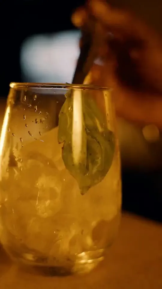Cocktail with basil leaf and crushed ice in warm light